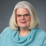 head shot of smiling woman with medium length straight light hair wearing glasses