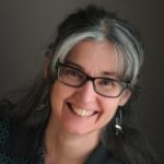 headshot of a smiling women wearing dark framed glasses