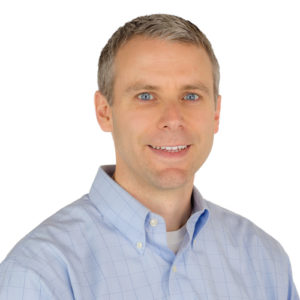 Headshot of a smiling man with short hair in a plaid button down shirt