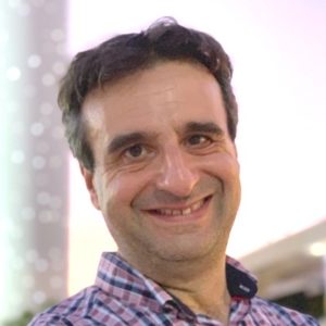 Headshot of a smiling man with short hair in a plaid button down shirt