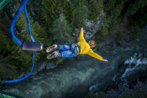 Young person bungee jumping off bridge into a forested river