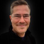 headshot of smiling man with short dark hair and glasses