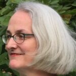 profile headshot of a smiling women with short grey hair and glasses