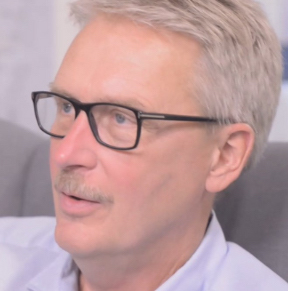 Headshot of man with short light hair and mustache and glasses